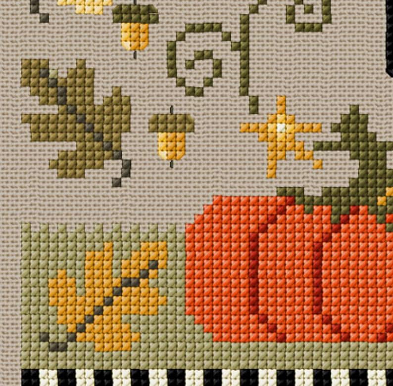 May include: Cross-stitch design featuring autumn elements. An orange pumpkin is next to a green and yellow leaf. Acorns and a star are above the pumpkin. The background is a light tan color with a black and white striped border.
