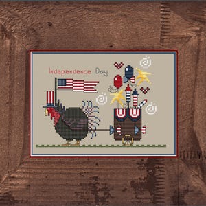 Può includere: Schema di ricamo a punto croce con un tacchino che tira un carro pieno di fuochi d'artificio e palloncini. Il carro è decorato con bandierine rosso, bianco e blu. Il tacchino indossa un cappello a cilindro rosso, bianco e blu. Il testo "Independence Day" è ricamato sopra il tacchino.