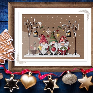 May include: A framed cross-stitch depicting three Christmas gnomes in festive attire, set in a snowy landscape. The artwork includes lanterns, snowflakes, and decorative details. A gingerbread tree and baubles are in the foreground.