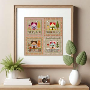 Può includere: Opera d'arte a punto croce incorniciata raffigurante quattro scene stagionali: Primavera, Estate, Autunno e Inverno. Ogni scena presenta una casa, alberi ed elementi stagionali. L'opera è in una cornice di legno ed è esposta su una mensola.