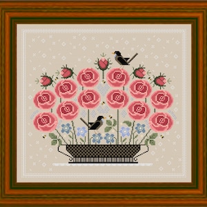 Può includere: Un ricamo a punto croce che presenta un bouquet di rose rosa in un vaso bianco e nero con due uccelli appollaiati sui gambi. Lo sfondo è un tessuto beige con un motivo bianco.