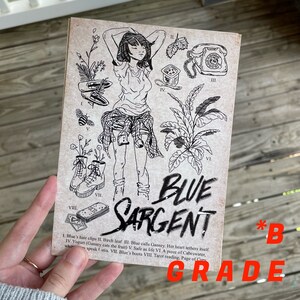 K&ouml;nnte beinhalten: Schwarz-wei&szlig;-Illustration einer Frau mit kurzen Haaren, die ein kariertes Hemd und Stiefel tr&auml;gt. Die Illustration ist von verschiedenen Symbolen umgeben, darunter ein Telefon, eine Pflanze, eine Biene, ein Blatt, eine Schachtel und Spielkarten. Der Text "BLUE SARGENT" ist in gro&szlig;en, stilisierten Buchstaben unter der Illustration geschrieben. Der Text "*B GRADE" ist in roten Buchstaben in der unteren rechten Ecke geschrieben.