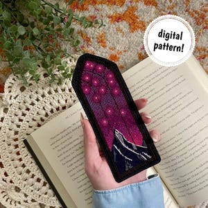 Könnte beinhalten: Handgefertigter Lesezeichen mit Kreuzstichmuster. Das Lesezeichen zeigt eine Berglandschaft mit Sternenhimmel in Lila- und Rosatönen. Der Text "digital pattern!" befindet sich in einem weißen Kreis.