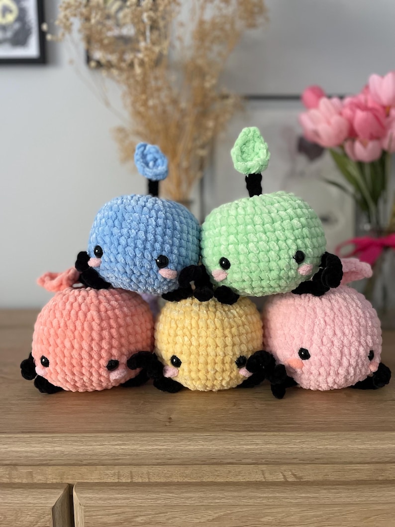 May include: Six crocheted plush toys shaped like whales in various pastel colors, including light blue, green, pink, yellow, and orange. Each whale has black eyes and a small crocheted fin on top.