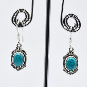 May include: A pair of silver earrings with turquoise stones set in an oval shape. The earrings have a delicate design and are perfect for everyday wear.