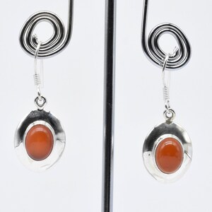 Könnte beinhalten: Ein Paar silberne Ohrringe mit orangefarbenen Karneol-Edelsteinen. Die Ohrringe haben ein schlichtes, rundes Design und sind perfekt für den Alltag.