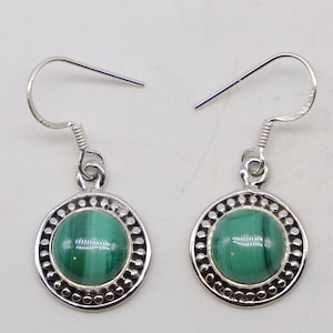 May include: A pair of silver-toned dangle earrings. Each earring features a round, polished, green malachite stone set within a decorative silver frame. The frame is encircled by small, evenly spaced silver beads. The earrings have a simple hook closure.
