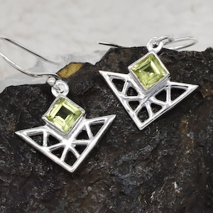 May include: A pair of silver earrings with geometric designs and green gemstones. The earrings are in the shape of a triangle with a smaller square gemstone in the center.