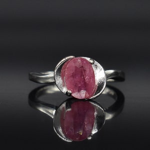 May include: A silver ring with a pink oval gemstone set in a delicate, twisted band.