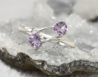 May include: A silver ring with two amethyst gemstones. The ring has a unique, twisted design.