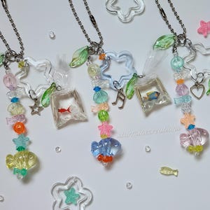 May include: Three clear acrylic fish-themed keychains with beaded accents. Each keychain features a fish-shaped charm, a small fish in a bag, and various colorful beads. The keychains are adorned with star and leaf charms.