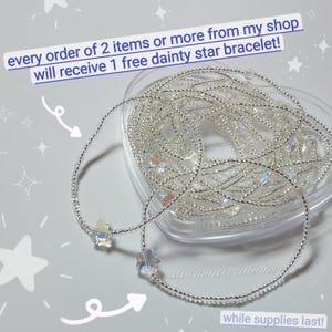 May include: Two delicate silver bracelets with star-shaped charms. The bracelets are displayed on a light gray surface, with a clear heart-shaped container filled with more bracelets in the background. Text on the image reads "every order of 2 items or more from my shop will receive 1 free dainty star bracelet!"