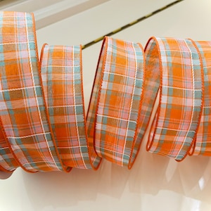 May include: Orange, white, and blue plaid ribbon with a subtle sheen. The ribbon is woven with a fine, delicate texture.