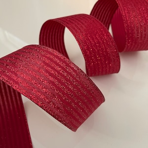 May include: Red ribbon with a glittery finish and thin white stripes. The ribbon is curled and folded.