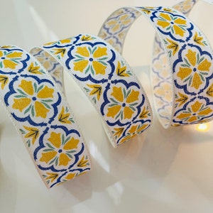 May include: White ribbon with a repeating pattern of yellow flowers with blue and green accents. The ribbon is curled and folded.
