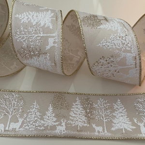 May include: A decorative ribbon with a winter forest scene. The ribbon features a beige background with white and gold accents. The design includes trees and deer, with a gold trim along the edges. The ribbon is rolled up.