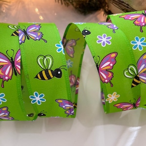 May include: Green ribbon with a repeating pattern of butterflies, bees, and flowers. The butterflies are purple, pink, and yellow. The bees are black and yellow. The flowers are blue, white, and purple.