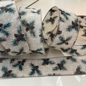 May include: A beige ribbon with a repeating pattern of pine branches and pine cones. The pine cones are brown with a hint of gold glitter. The pine branches are a teal green color.
