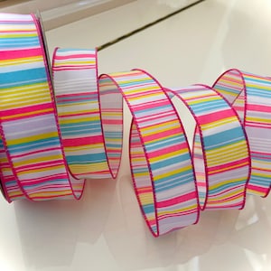 May include: A pink, white, yellow, blue, and purple striped ribbon with a pink edge.