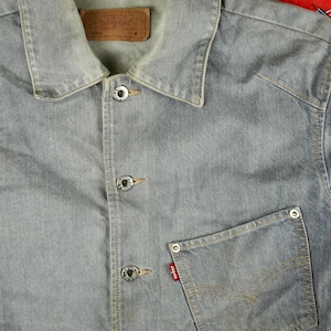 Op de afbeelding: Lichtblauwe spijkerjas met een klassieke kraag en knoopsluiting. Voorzien van een borstzak met een rood Levi's label en zilveren knopen. Een jas in vintage stijl, geschikt voor dagelijks gebruik.