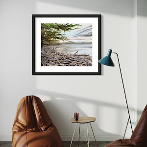 May include: A framed landscape art print depicting a coastal scene with driftwood, a tree, and a body of water under a cloudy sky. The artwork is in a black frame and hangs on a white wall. The room also features a brown leather chair, a small table, and a teal floor lamp.