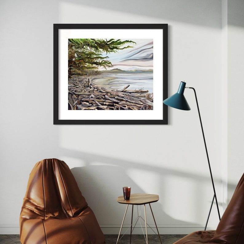 May include: A framed landscape art print depicting a coastal scene with driftwood, a tree, and a body of water under a cloudy sky. The artwork is in a black frame and hangs on a white wall. The room also features a brown leather chair, a small table, and a teal floor lamp.