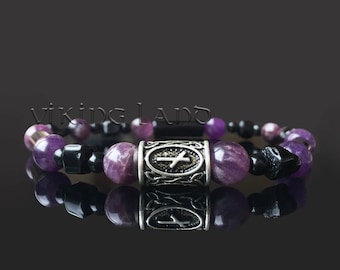 May include: A purple and black beaded bracelet with a silver charm featuring a cross design. The bracelet is on a black reflective surface.