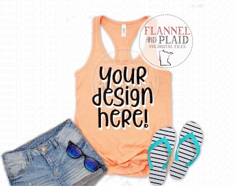 May include: A peach-colored tank top with the text "your design here!" printed on the front. The tank top is laying on a white surface with a pair of blue denim shorts and a pair of blue and white striped flip flops.
