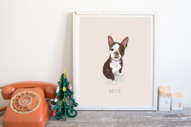 May include: Framed art print featuring a Boston Terrier dog illustration. The dog is brown and white, with the name "Bosco" below. The artwork is set against a pale pink background, in a white frame. A vintage orange telephone and a green Christmas tree are in the foreground.