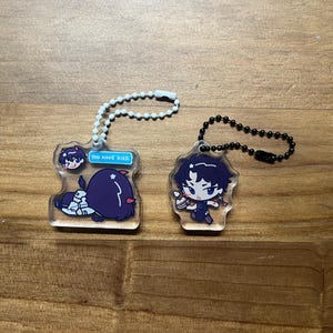 Könnte beinhalten: Zwei Schlüsselanhänger aus Acryl mit Cartoon-Charakter-Designs. Ein Schlüsselanhänger zeigt einen Charakter mit dem Text "You have died". Der andere Schlüsselanhänger hat einen Charakter, der einen kleinen Gegenstand hält. Beide Schlüsselanhänger haben eine Kette zur Befestigung.