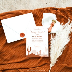 May include: A baby shower invitation with a desert theme. The invitation features a tan background with a silhouette of a desert landscape with cacti and a sunset. The text on the invitation reads "Please join us for a baby shower in honor of Leyna Hansley. Saturday, February 25th at 3pm. Olive & Ivy - 7135 E Camelback Rd Scottsdale, AZ. RSVP by February 1st - laurabergmandesign@gmail.com. Registered at Target and Amazon."