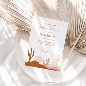 May include: A white baby shower invitation with a desert landscape design. The invitation features a cactus, a sunset, and the text "PLEASE JOIN US FOR A baby shower in honor of Leyna Hansley Saturday, February 26th at 3pm Olive & Ivy 7135 E Camelback Rd Scottsdale, AZ RSVP by February 1st-laurabergmandesign@gmail.com Registered at: Target and Amazon"
