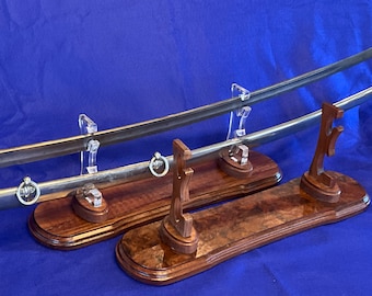 Puede incluir: Dos espadas expuestas en soportes de pared de madera con soportes para espadas de acrílico transparente. Las espadas tienen empuñaduras de metal y se exhiben sobre un fondo azul.