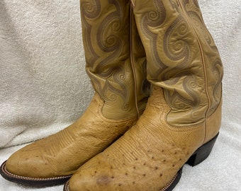 May include: A pair of tan ostrich leather cowboy boots with a decorative swirl pattern on the shaft. The boots have a pointed toe and a brown leather sole.