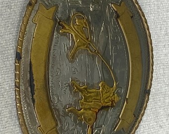 May include: Silver and gold tone belt buckle featuring a cowboy riding a bucking bronco. The buckle is oval shaped and has a decorative border.