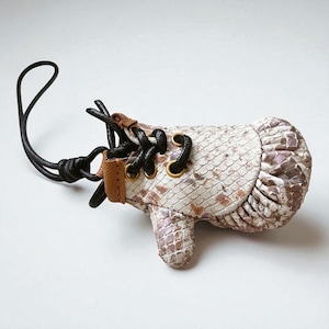 May include: A small, novelty leather shoe-shaped keychain. The keychain features a snakeskin pattern in shades of white, brown, and purple. It has black laces, gold eyelets, and a brown leather strap. A black loop is attached.