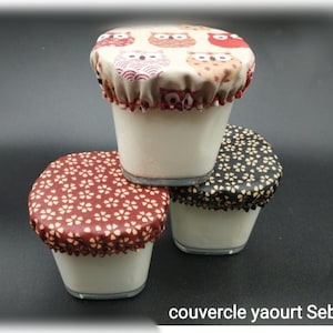 May include: Three glass jars with white yogurt, each topped with a fabric cover. The covers are different patterns: owls, red and white flowers, and black and white flowers. The text "couvercle yaourt Seb" is at the bottom of the image.