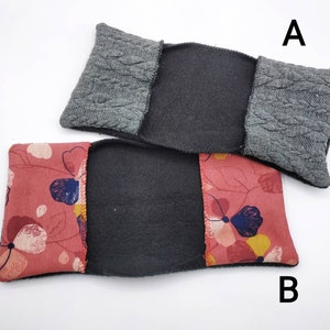 Könnte beinhalten: Zwei Stoff-Kissenbezüge, einer grau mit einem Zopfmuster und einer mit einem Blumendruck in den Farben Rosa, Rot und Blau. Die Bezüge sind reversibel, mit einem schwarzen Fleece-Futter auf der Innenseite.