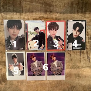 May include: A collection of six photo cards featuring images of young men. The cards are rectangular, with varying backgrounds and poses. Some cards have a white border, while others have a red or black border. The cards are arranged on a wooden surface.