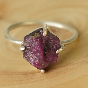 May include: A silver ring with a raw, faceted ruby gemstone. The ruby is a deep, rich red color and has a natural, irregular shape.