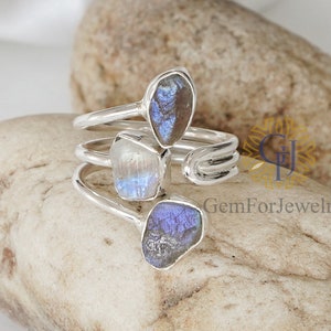 May include: A silver ring featuring three iridescent labradorite stones. The stones are set in a twisted band and display a range of blue, grey, and white hues.