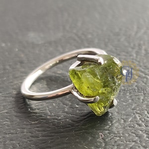 Puede incluir: Un anillo de plata con una piedra de peridoto verde en bruto engastada en garras.