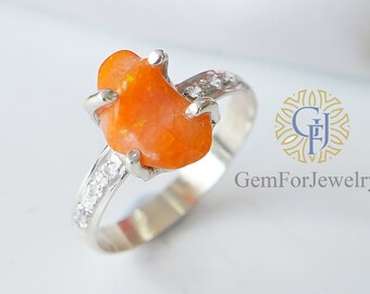 Puede incluir: Un anillo de plata con una gran piedra preciosa naranja engastada en una garra. La banda está adornada con pequeñas piedras transparentes.