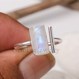 May include: A silver ring with a rectangular moonstone and a silver bar accent. The ring is on a finger.