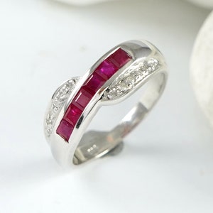 May include: A silver band ring with a row of red ruby stones and smaller clear stones set in the band.