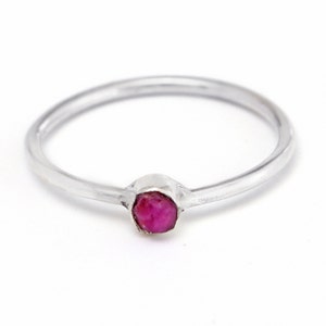 May include: A simple silver band ring with a small, faceted ruby gemstone.
