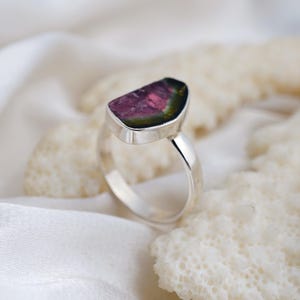 K&ouml;nnte beinhalten: Ein Silberring mit einem Wassermelonen-Turmalin-Edelstein. Der Edelstein zeigt rosa, gr&uuml;ne und schwarze Farbt&ouml;ne. Der Ring hat ein poliertes Band und eine L&uuml;nettenfassung. Ein Schmuckst&uuml;ck.
