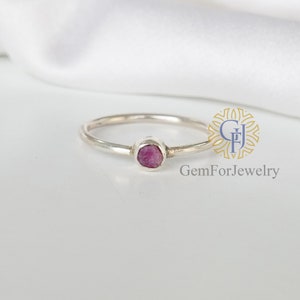 May include: A delicate silver ring with a small, faceted pink gemstone set in a bezel setting. GemForJewelry is printed below the ring.