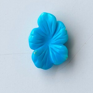 May include: A turquoise blue flower carved from stone. The flower has five petals and a center hole.