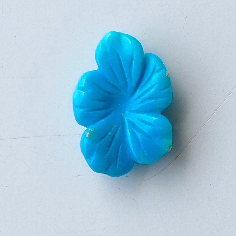 May include: A turquoise blue flower carved from stone. The flower has five petals and a center hole.